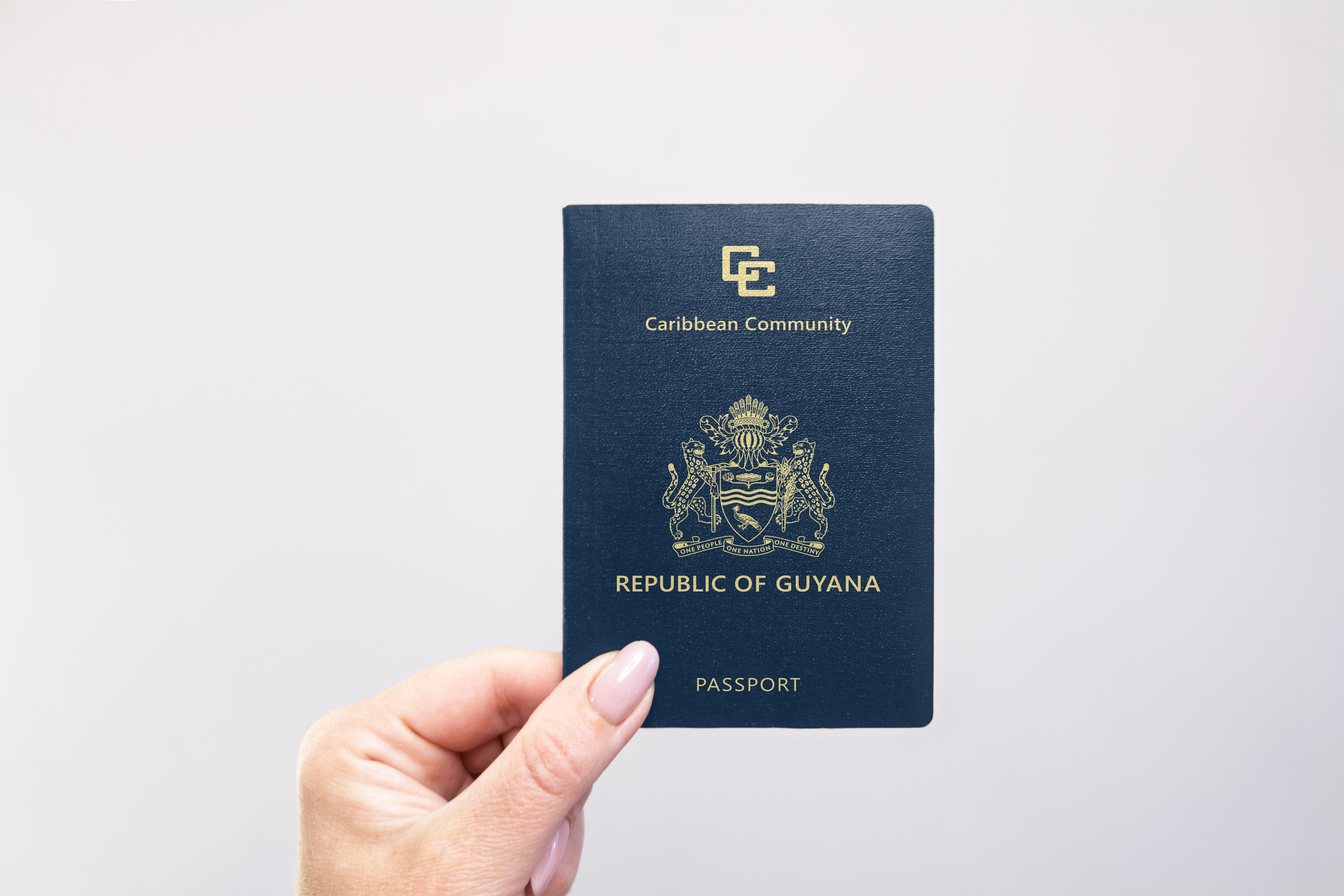 Guyana Passport Held In Hand Against A Plain White Background